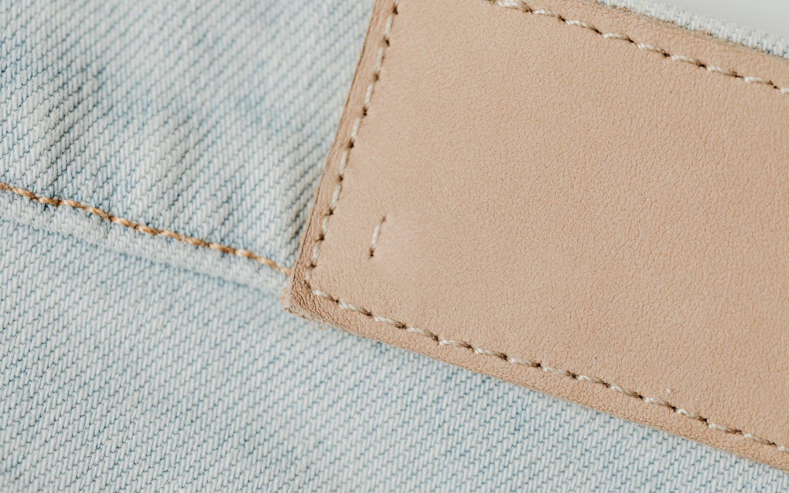 Close-up of a blank leather patch stitched onto light blue denim fabric