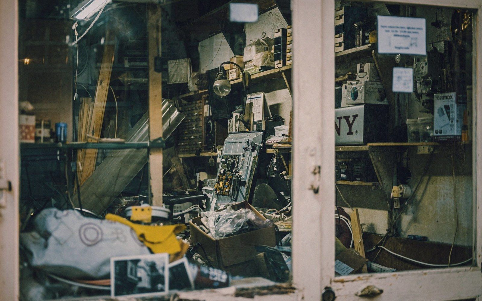 Cluttered repair shop window filled with electronics, tools and cardboard boxes on shelves