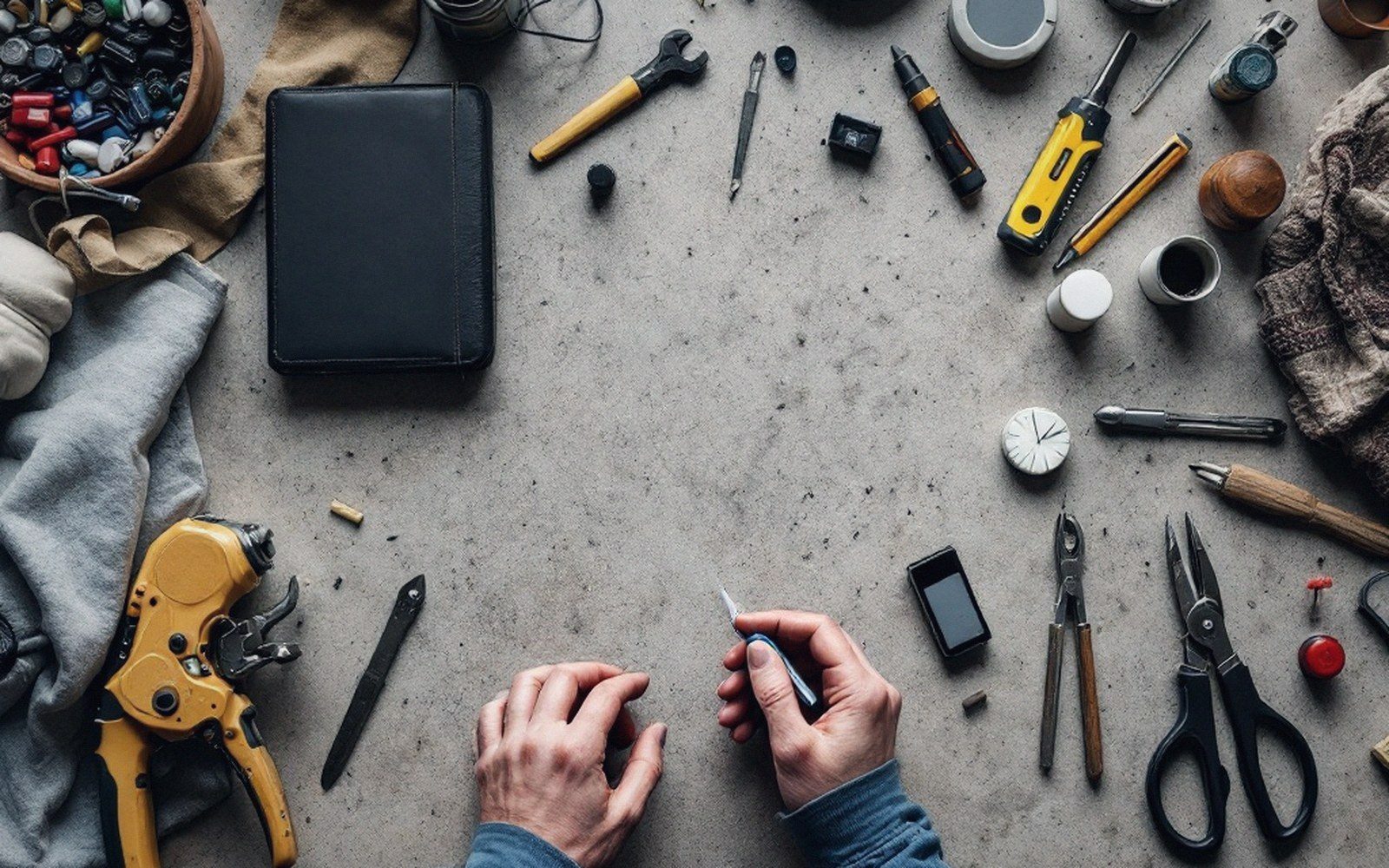 Hands holding a small tool surrounded by leather goods and repair tools on a workbench