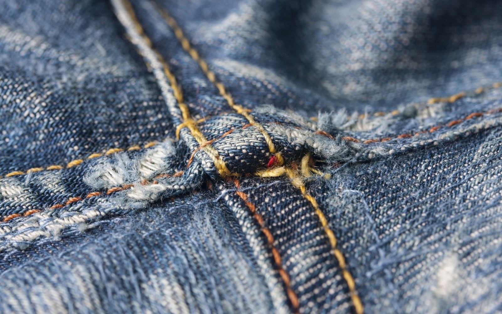 Close-up of frayed denim seam with visible stitching wear at a worn crotch seam