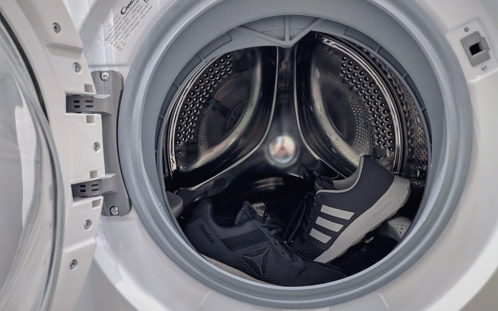 A pair of sneakers sitting inside the drum of a front-loading washing machine