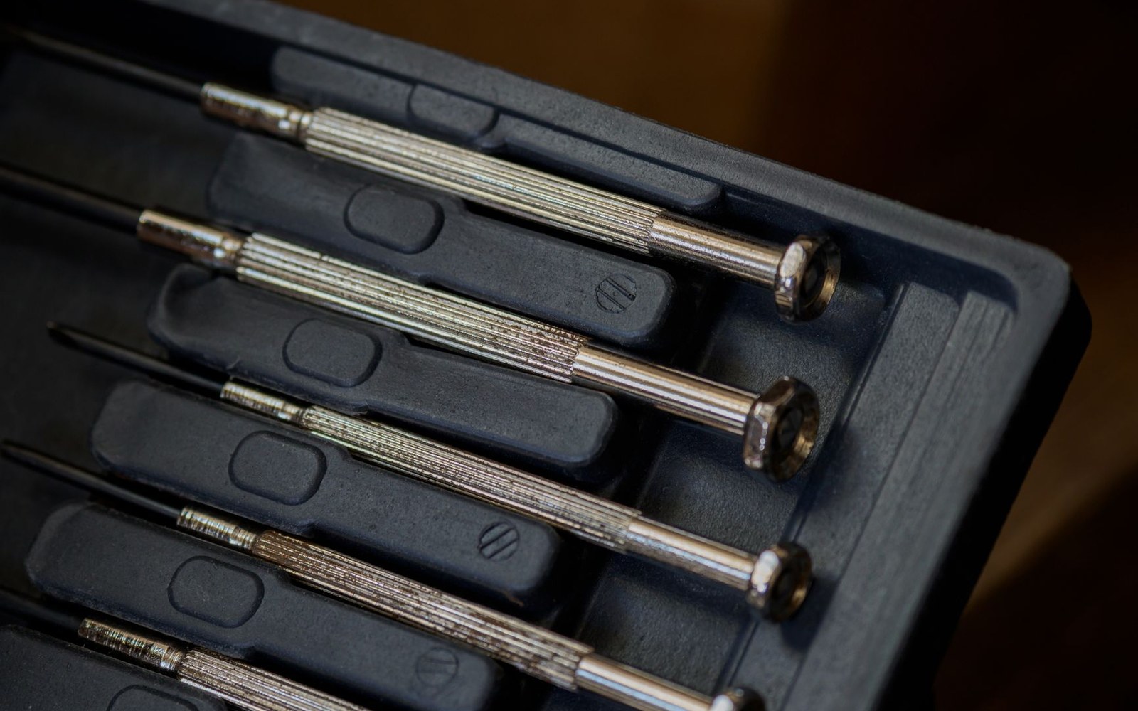 Set of small precision screwdrivers with knurled handles arranged in a black tray