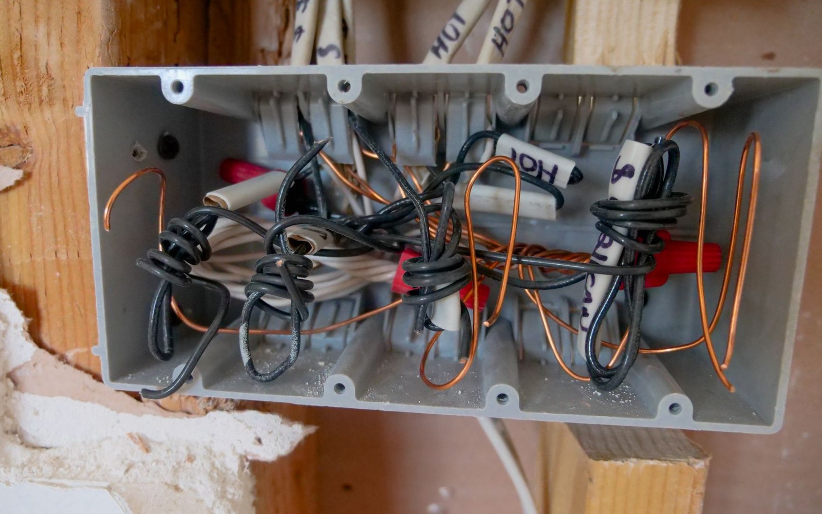 Electrical junction box with tangled copper and black wires mounted in wall studs